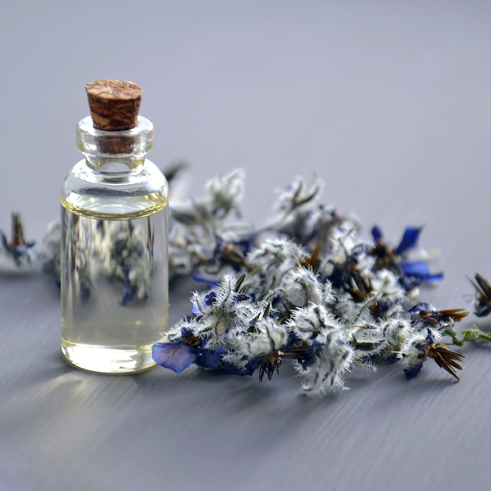 An essential oil in a vial or cork bottle with a plant branch that has flowers on it over the gray flat surface
