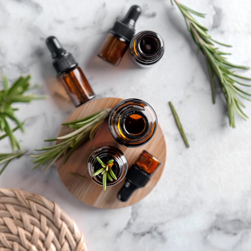 Bottles with rosemary essential oil on light background, top view