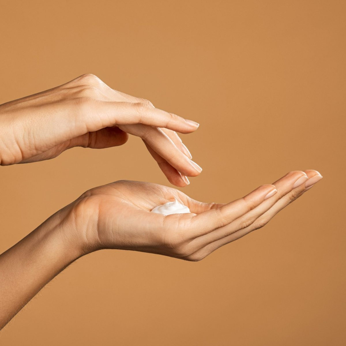 Close up shot of beautiful female hands holding and applying moisturiser. Beauty woman hand applying cream. Beautiful girl on creamy background holding moisturizer.