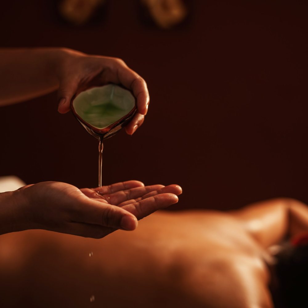 Masseur pouring aroma oil on hand, for massage on back of customer. Relaxation young male customer get service aromatherapy massage with masseuse in spa salon. Aromatherapy massage, Selective focus.