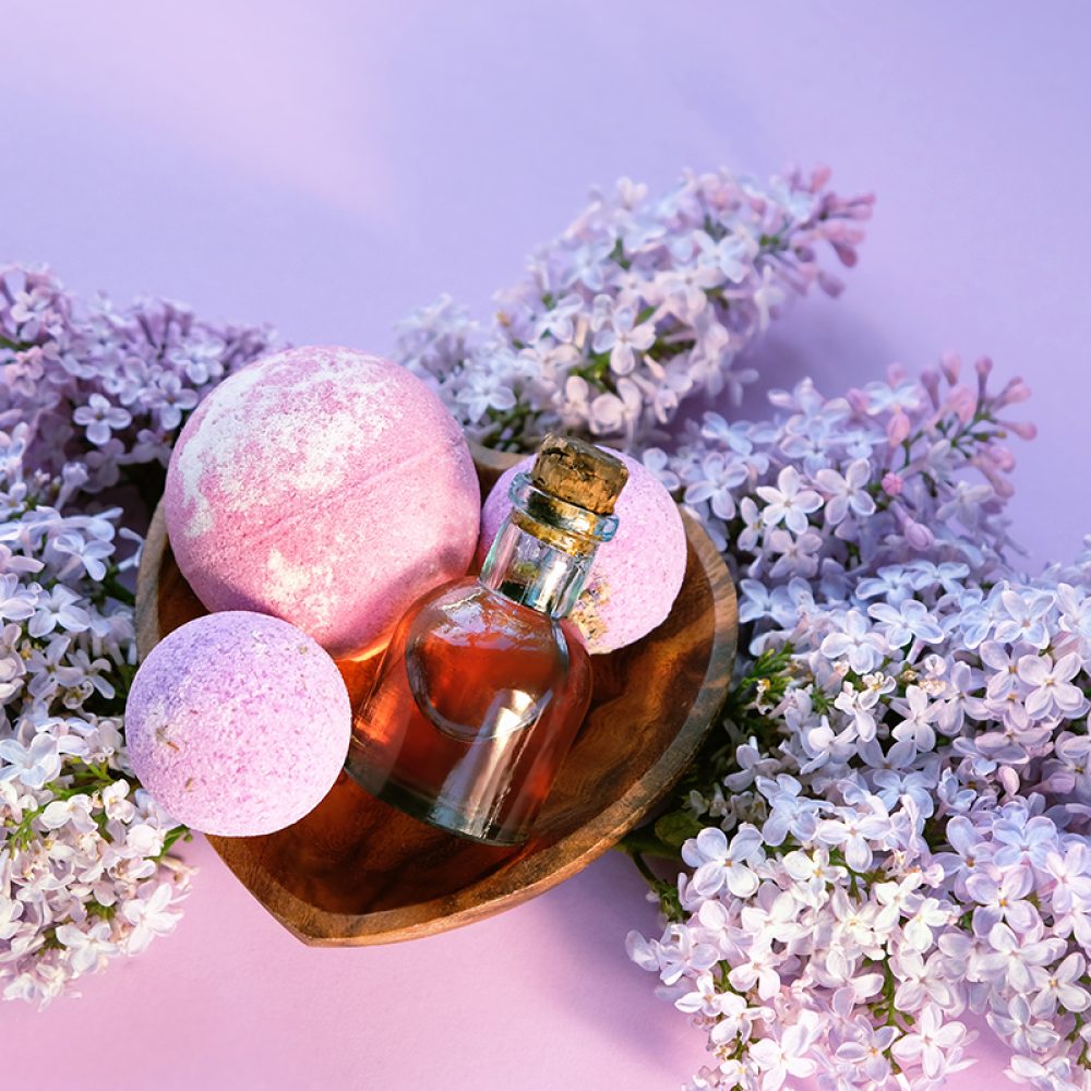 essential oil bottle, bath bombs and lilac flowers on abstract v